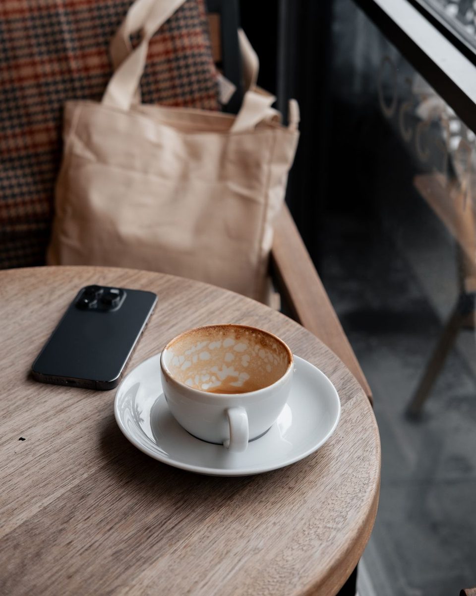 木の丸テーブルに置いたカフェラテとスマートフォン